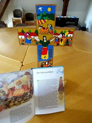 Buntes Kreuz aus Bauklötzen neben einem offenen Kinderbuch.