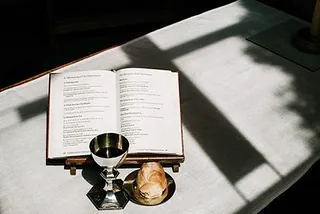 Kelch und Brot neben einem offenen Buch auf einem Altar.