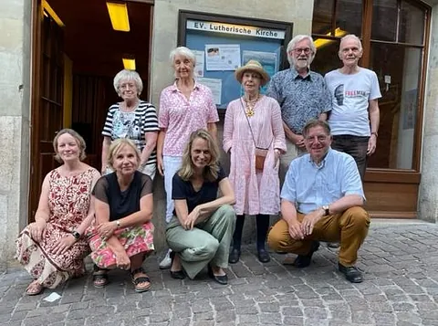 Eine Gruppe von neun Personen posiert vor der Evangelisch-Lutherischen Kirche.